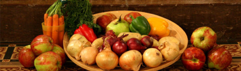 A basket of colorful vegetables sitting on table in between two piles of apples and carrots.