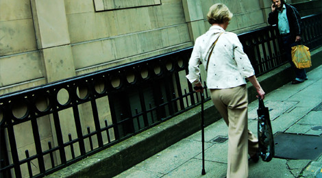 A woman using a cane walks down a city sidewalk.