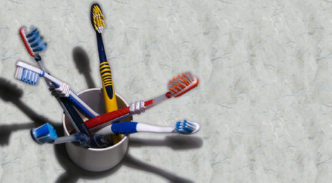 Multiple-colored toothbrushes sit in a cup on a bathroom counter.