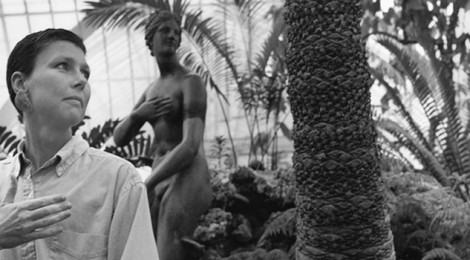 Stephanie Byram, who died from breast cancer at the age of thirty-eight, mimics the pose of a statue in a tropical greenhouse setting.